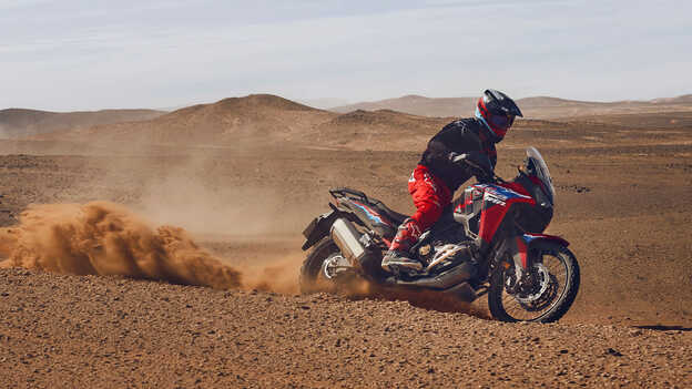 Fotómodell ül egy CRF1100L Africa Twin motorkerékpáron a sivatagban.